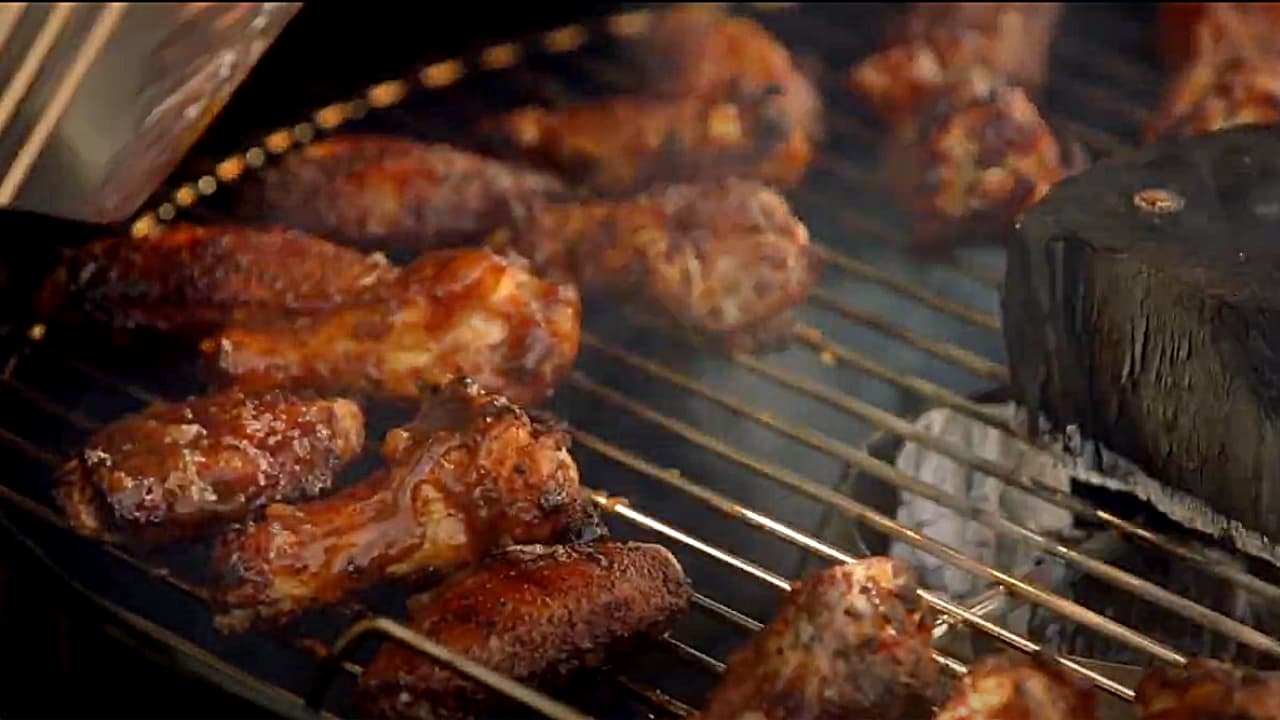 A close-up view of glazed chicken wings cooking on a metal barbecue grill grate over hot coals.