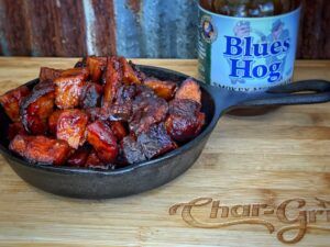 Cast Iron Skillet filled with cooked burnt end brisket on a cutting board with BBQ sauce on the side