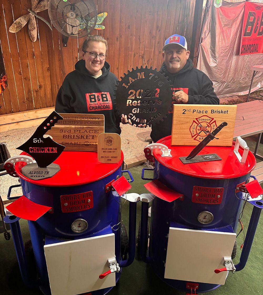 B&B Team pitmasters Mark Pugh behind red-and-blue barbecue smokers at an indoor booth display.