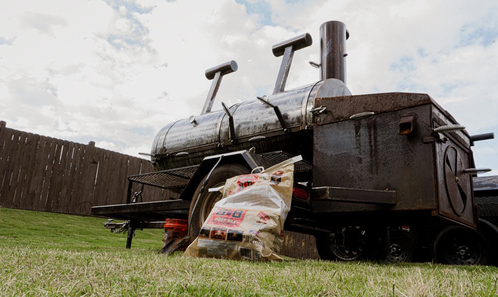 Smoker with bag of B&B Post Oak mini logs in grassy backyard