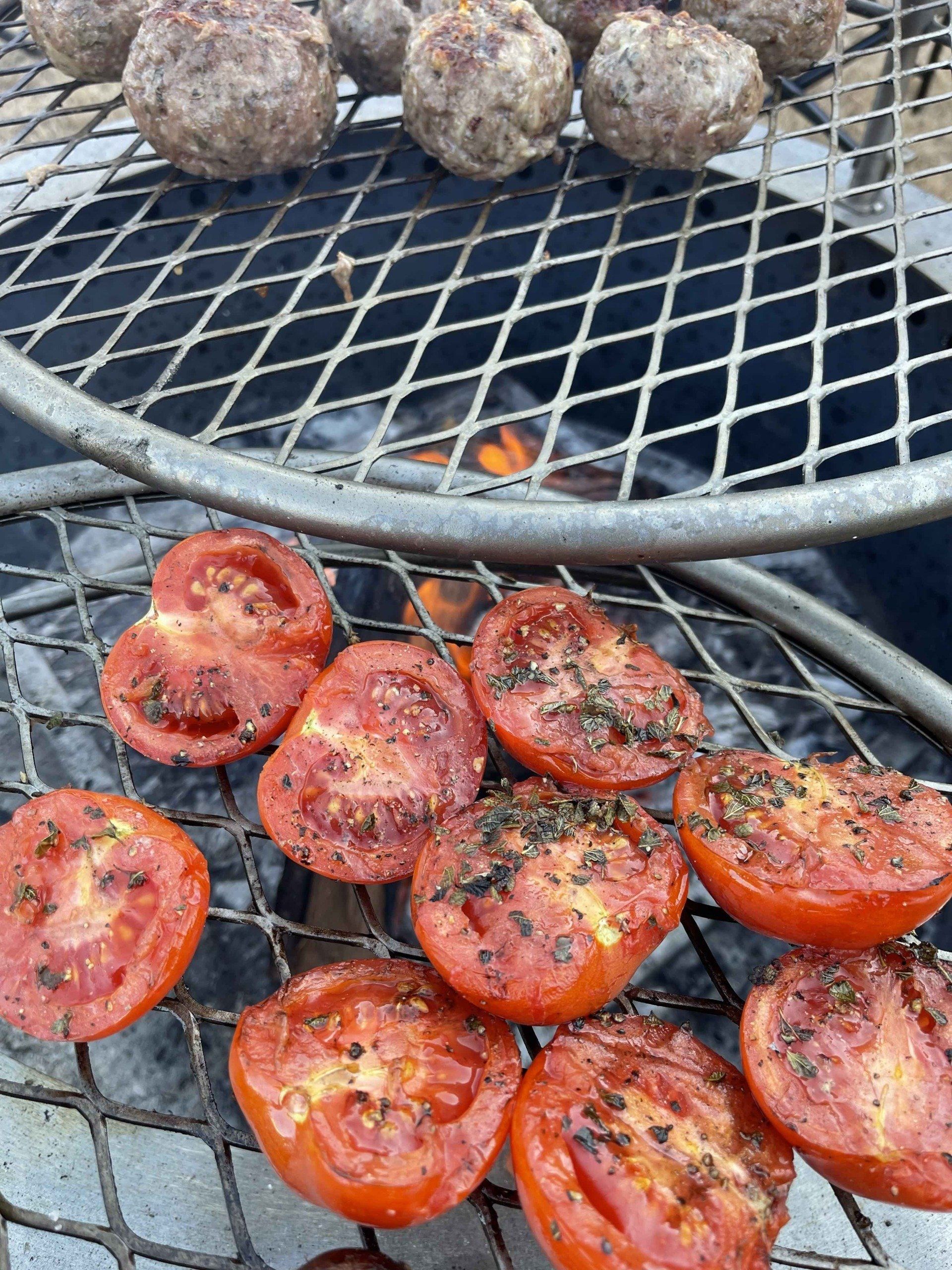 Tomatoes and stuffed meatballs cooking on the grill