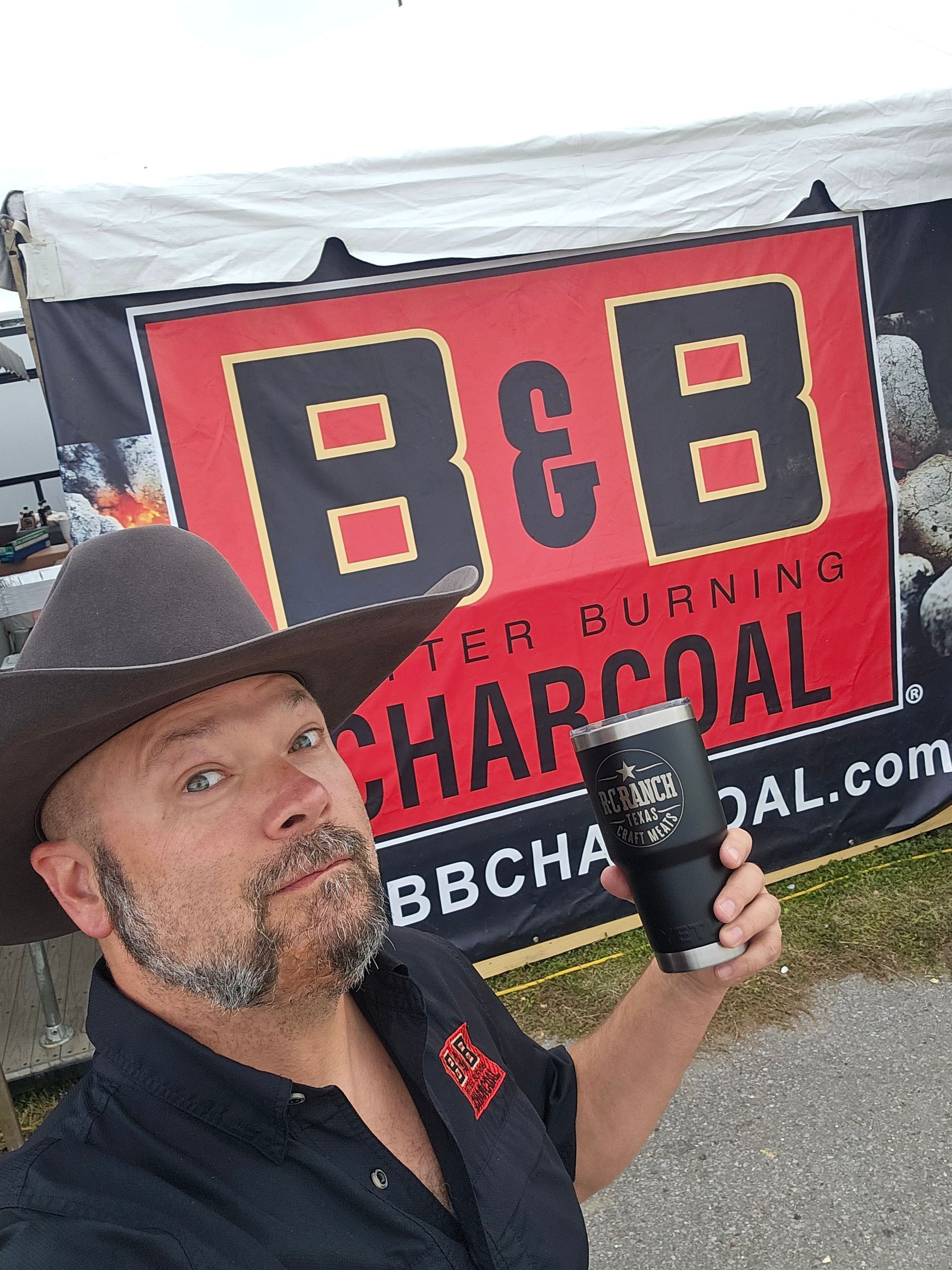 B&B Ambassador and Pitmaster Mark Lambert is holding a trophy on stage at a BBQ competition