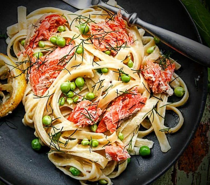 Fettuccine alfredo with peas & grilled salmon, on plate with fork, garnished with a grilled lemon slice