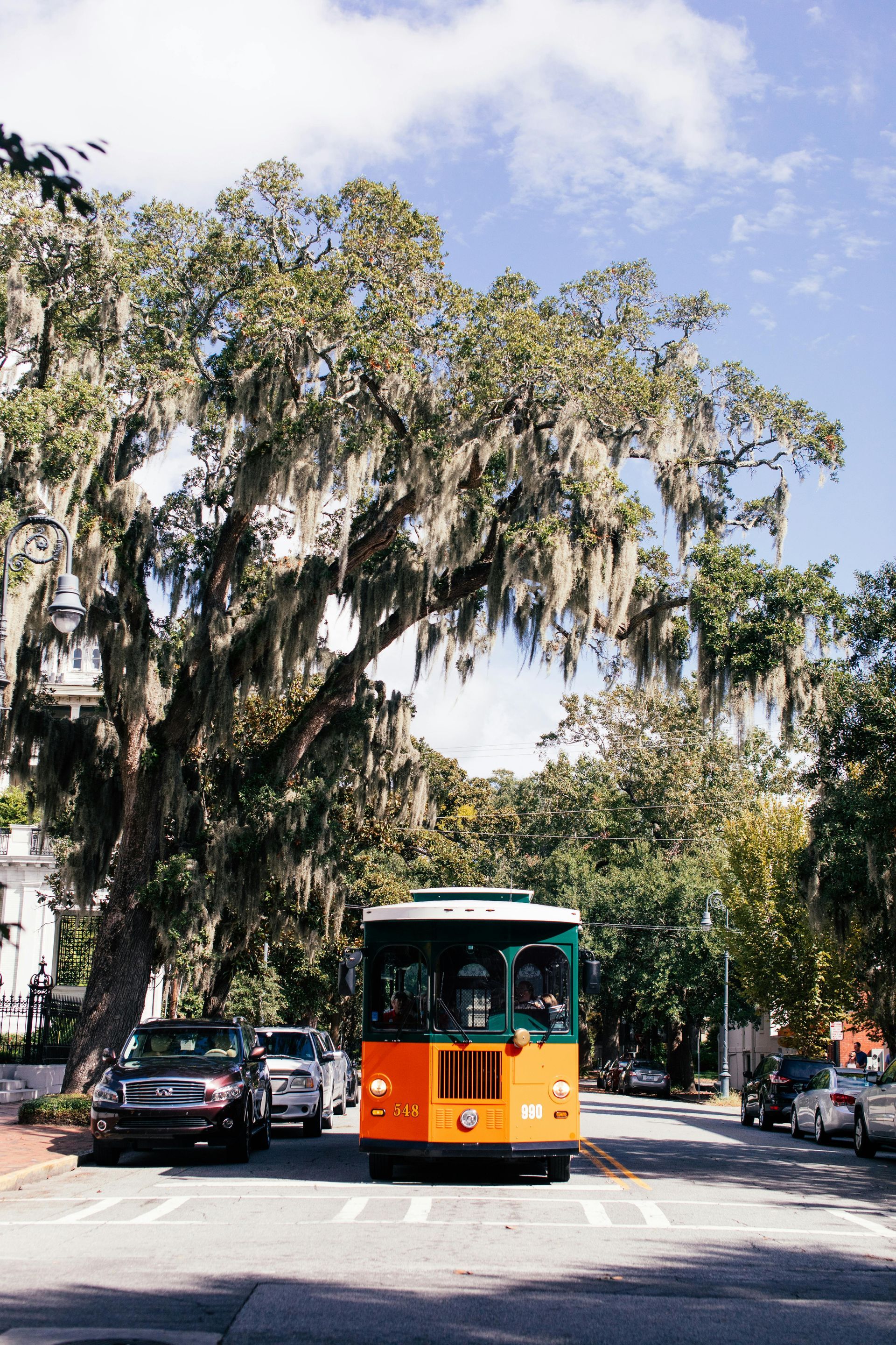 An orange and green trolley is driving down a street.