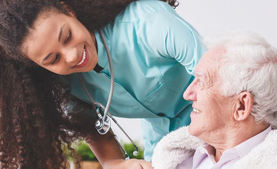 A nurse is listening to an elderly man 's heartbeat with a stethoscope.
