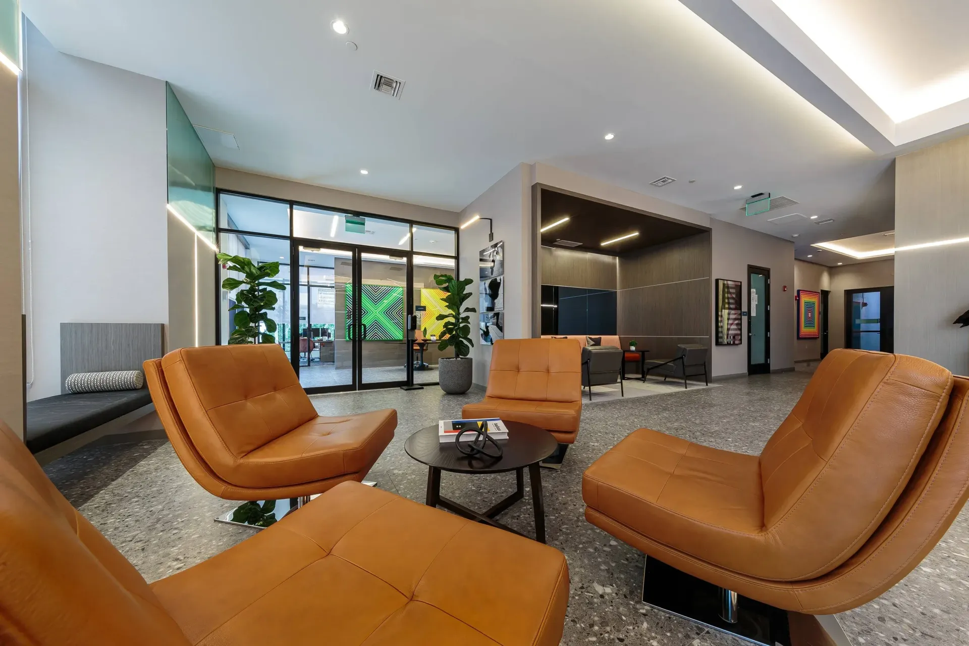 Modern apartment lobby with orange leather lounge chairs, glass entry doors, and greenery.