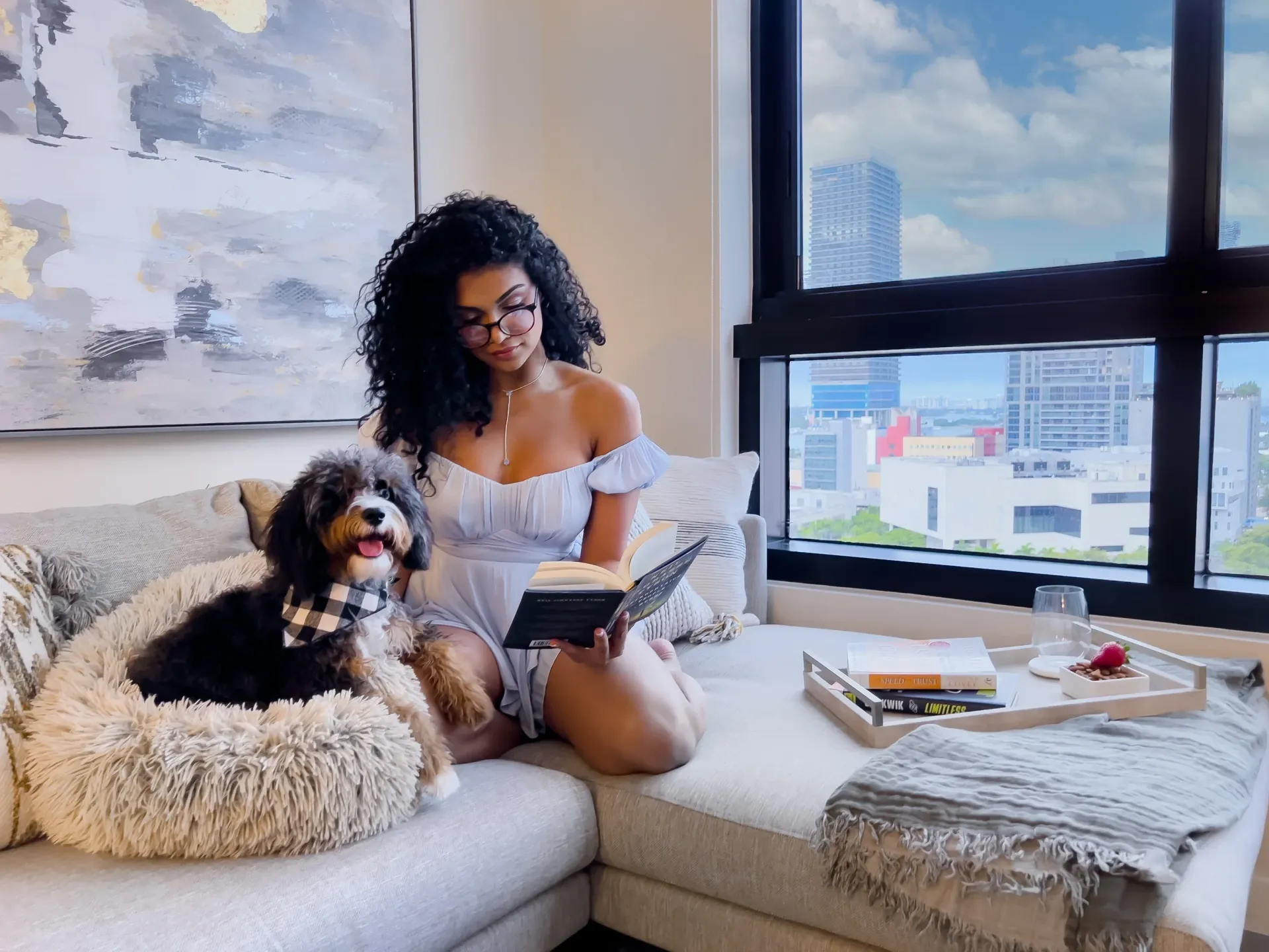Woman sitting on a sofa reading a book with a dog in a modern apartment living room.