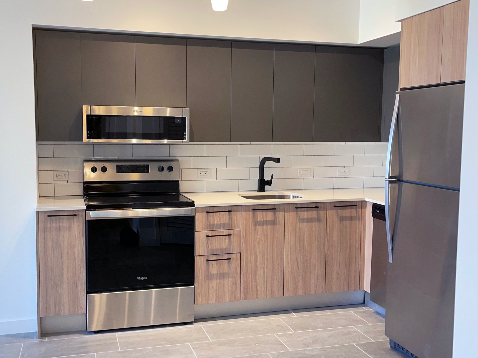 Modern kitchen with stainless-steel appliances, dark upper cabinets, wood-toned lowers, and a black faucet.