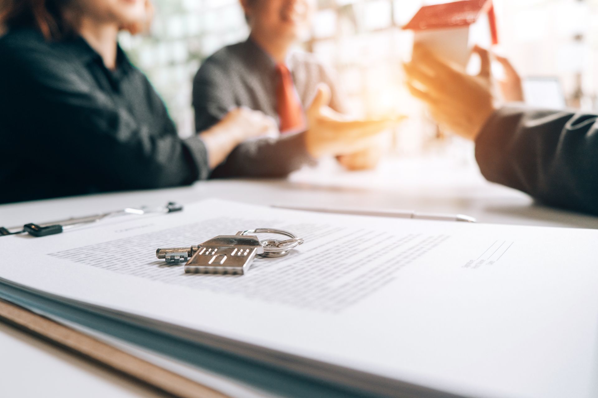 A couple of people are sitting at a table with a house model and keys on top of a piece of paper.