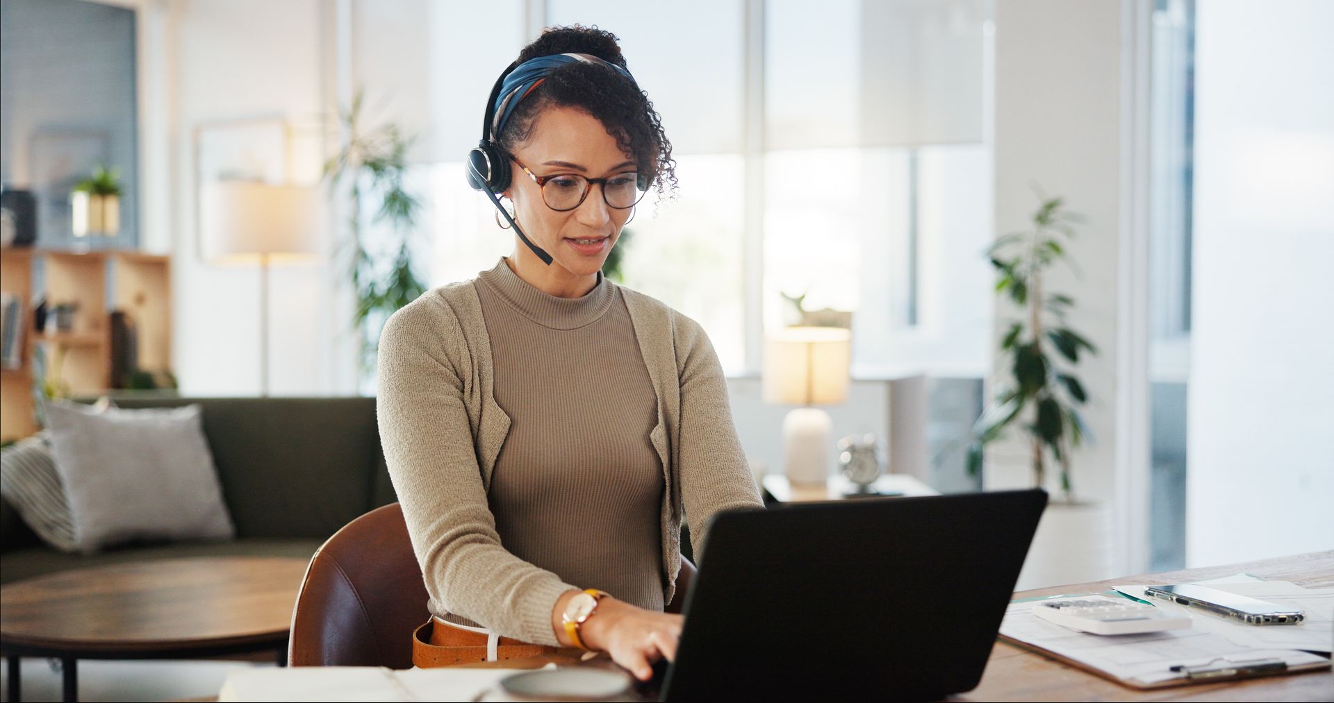 A woman wearing a headset is sitting at a desk using a laptop computer.