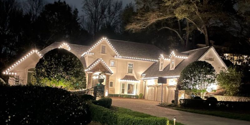 House at night decorated with white holiday lights and glowing windows, viewed from the front yard