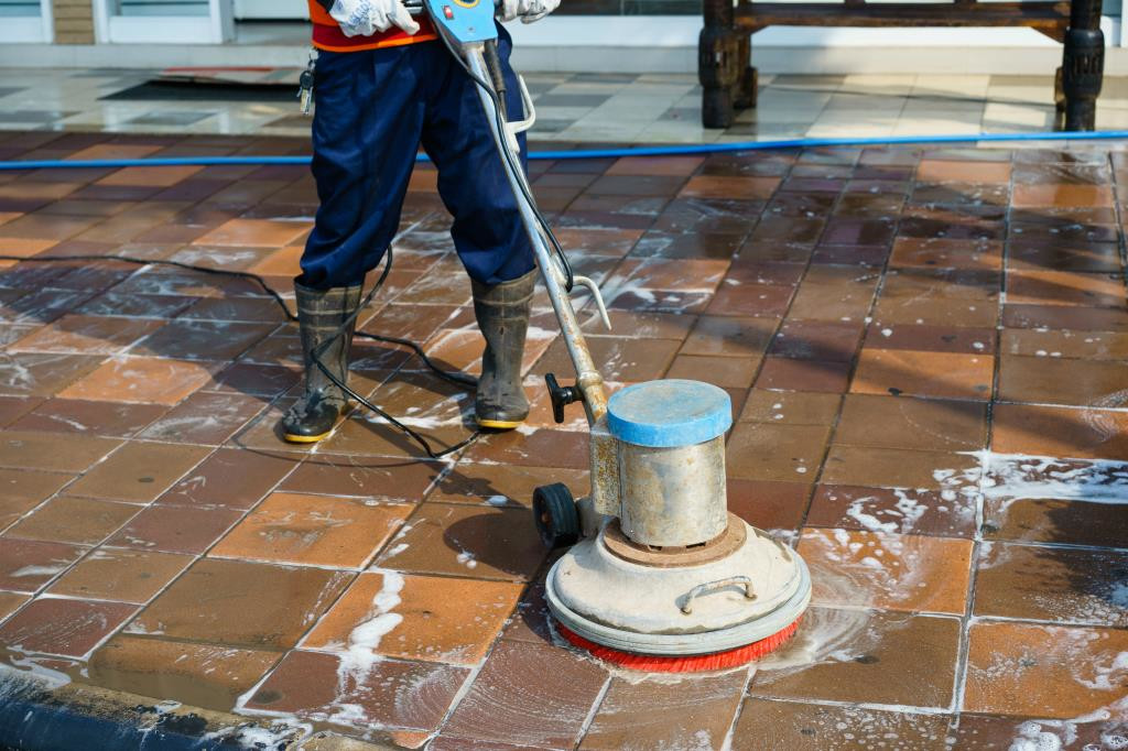 Worker pressure-washing a wet brick patio with a floor scrubber and hose