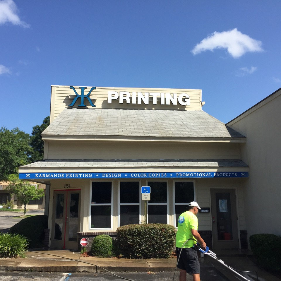 Printing shop storefront with blue awning and a worker in a neon vest walking past