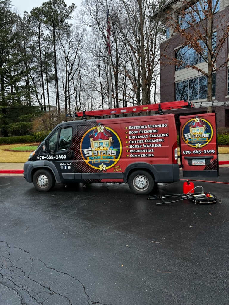 Red promotional van parked on wet pavement beside a brick building, with a sign trailer attached.