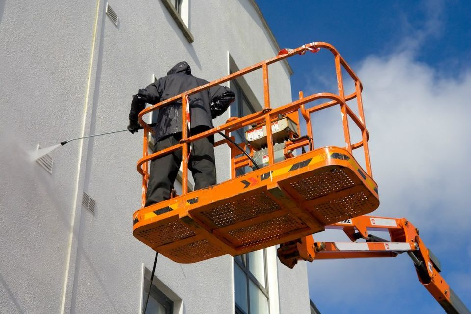 Worker on an orange lift painting a building wall near the roofline