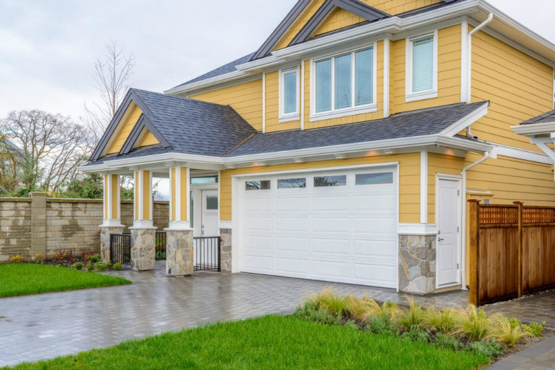 Yellow two-story house with white garage, stone accents, and wet driveway after rain