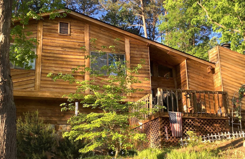 Wooden cabin with a porch amid trees and greenery in warm sunlight