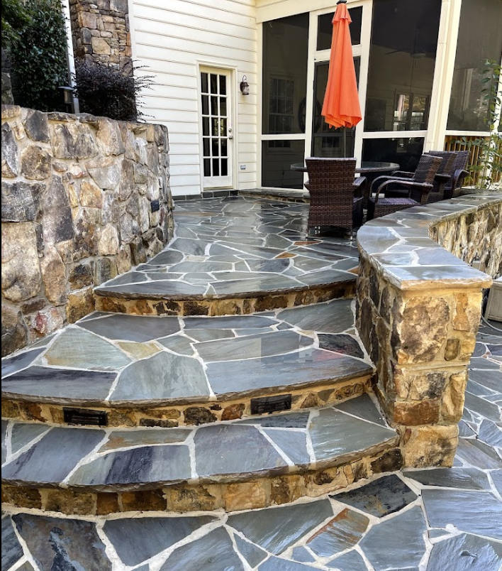 Stone patio steps with slate pavers leading to a backyard porch and orange umbrella