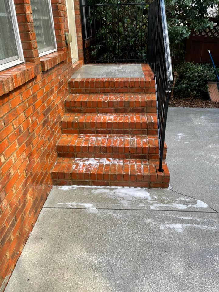 Brick front steps with a black railing leading up to a house entrance