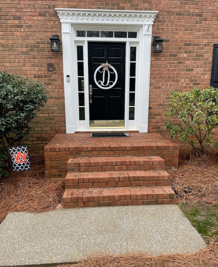 Brick townhouse entrance with black door, white trim, and brick steps above a concrete walkway.