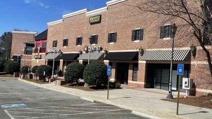Brick storefront with awnings and a parking lot in front on a sunny day