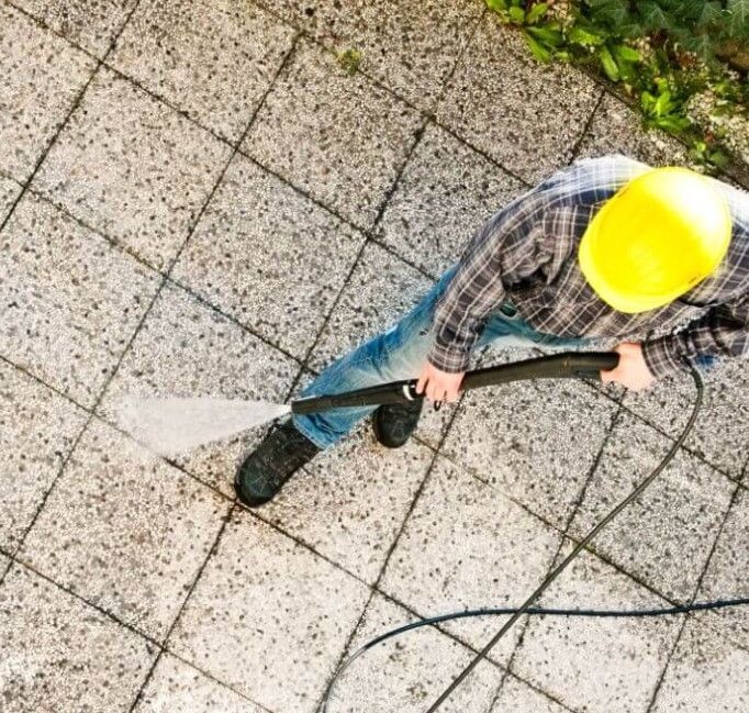 Worker in yellow hard hat spraying water on a tiled pavement with a hose from above
