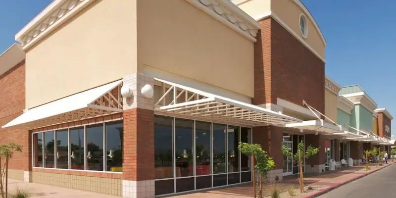 Strip mall storefront with brick and beige facades, glass windows, and awnings under a clear sky