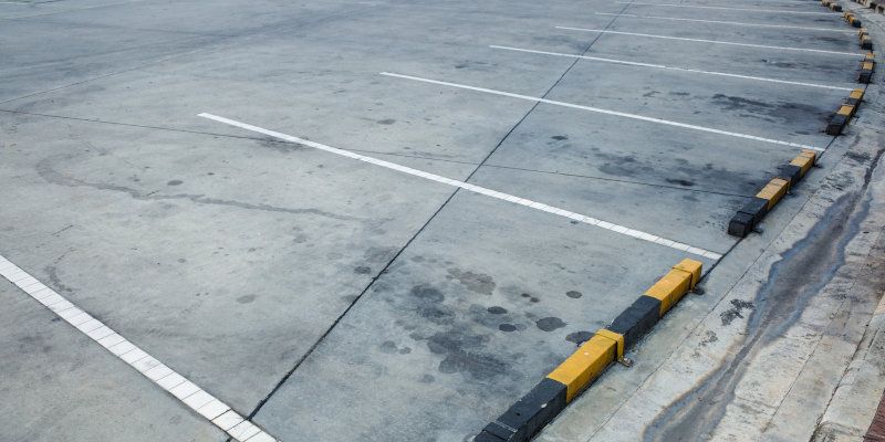Empty concrete parking lot with white lines and black-yellow curb stops