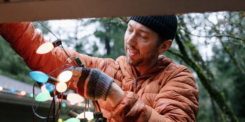 Man in an orange jacket hanging colorful holiday lights outdoors