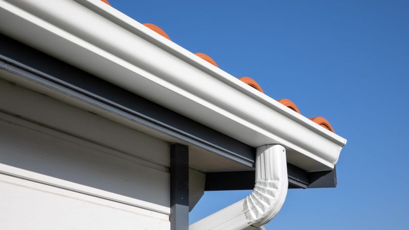 White house gutter and downspout under a tiled roof against a blue sky