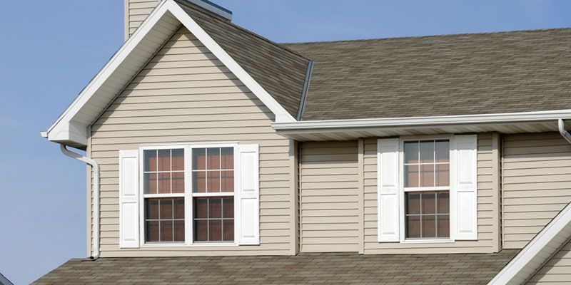Exterior of a beige house with white-trimmed windows and gray shingled roof