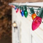 Colorful holiday string lights hanging along a white wall outdoors