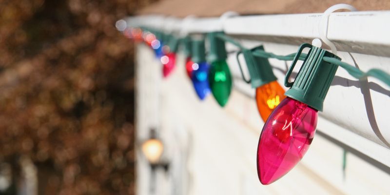 Colorful holiday string lights clipped along a white gutter outdoors