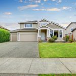 Suburban house with attached garage, wide driveway, and green front lawn under a partly cloudy sky