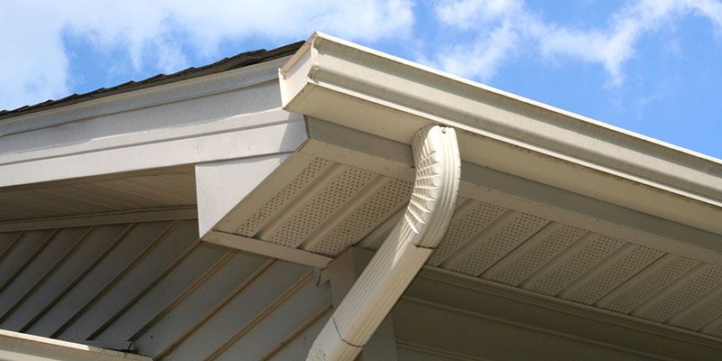 White rain gutter and downspout on a house roof against a blue sky