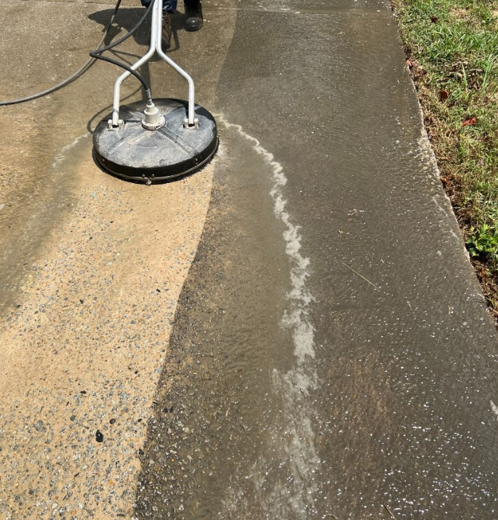 Pressure-washing a concrete sidewalk, cleaning a dirty strip beside the curb