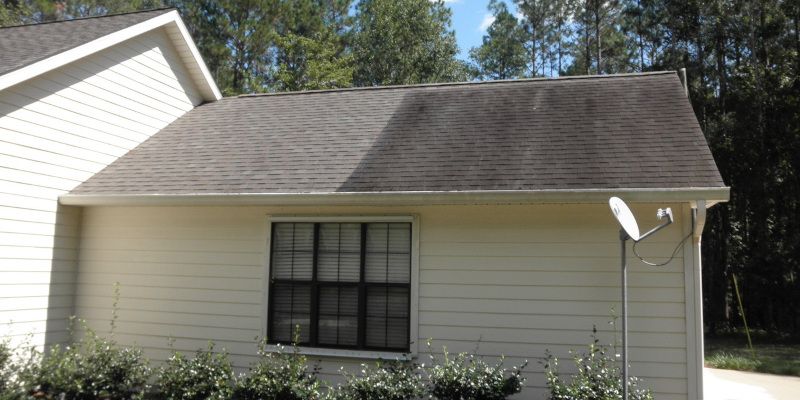 Small white house exterior with gray shingled roof and a satellite dish by the window.