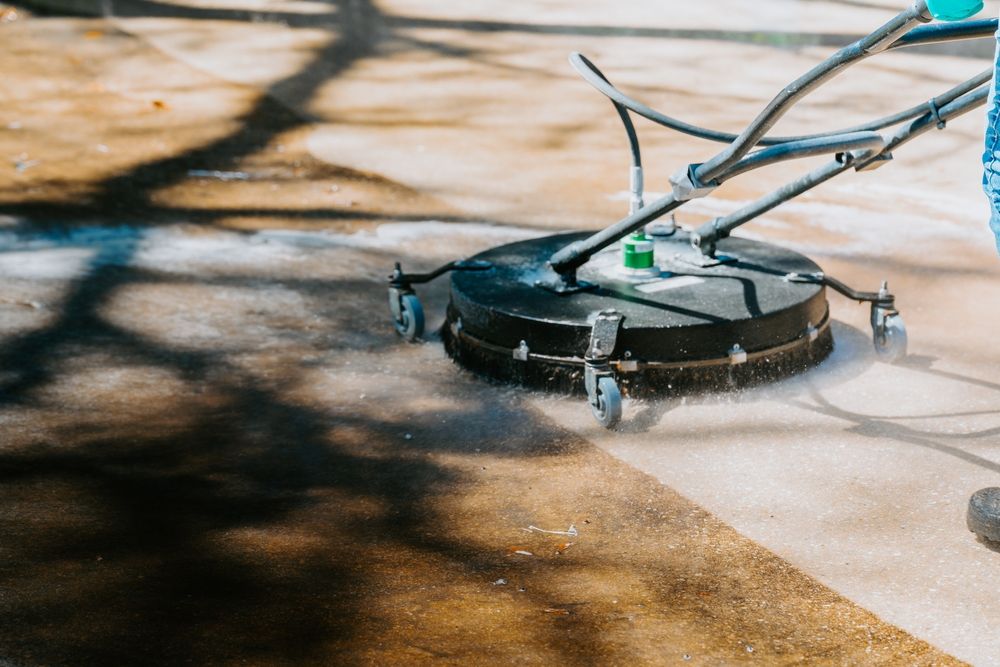 Round black cleaning robot on a wet concrete surface, spraying water in an outdoor area.
