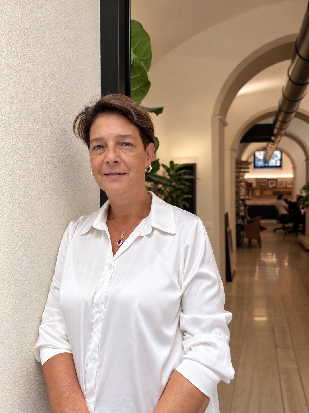 Donna con una camicia bianca in piedi in un luminoso corridoio con archi e piante