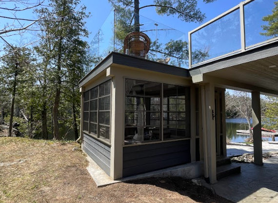 Modern cabin porch with dark trim, large windows, and a glass-railed deck in a wooded setting