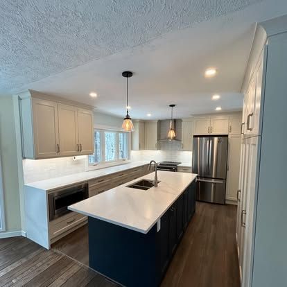 Modern kitchen with navy island, light countertops, stainless steel appliances, and wood flooring.