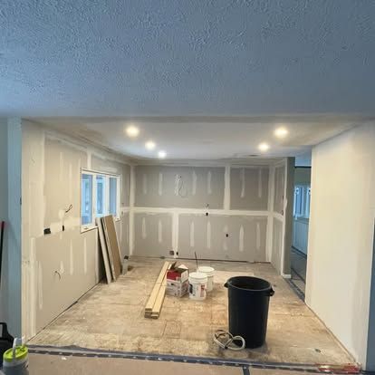 Interior of a room under construction with drywall installed, exposed floor, and overhead lighting.