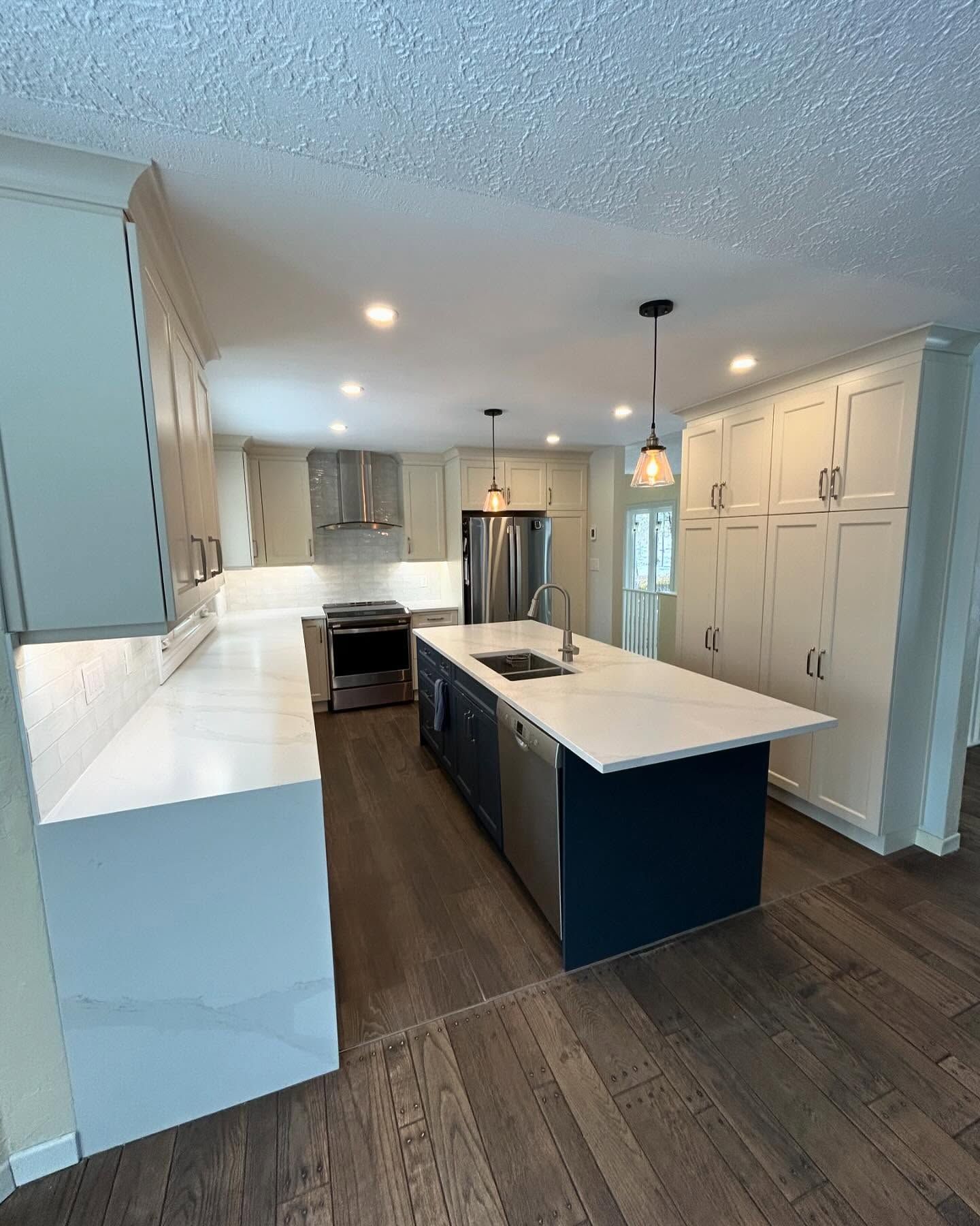 Modern kitchen with white and navy cabinets, island with sink, stainless steel appliances, and wood floor.
