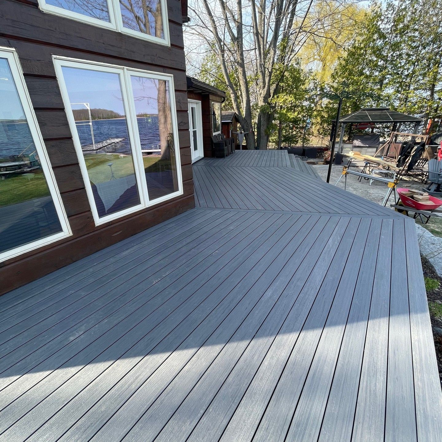 Gray composite deck extending from a brown house with large windows. Lake visible in the reflection.