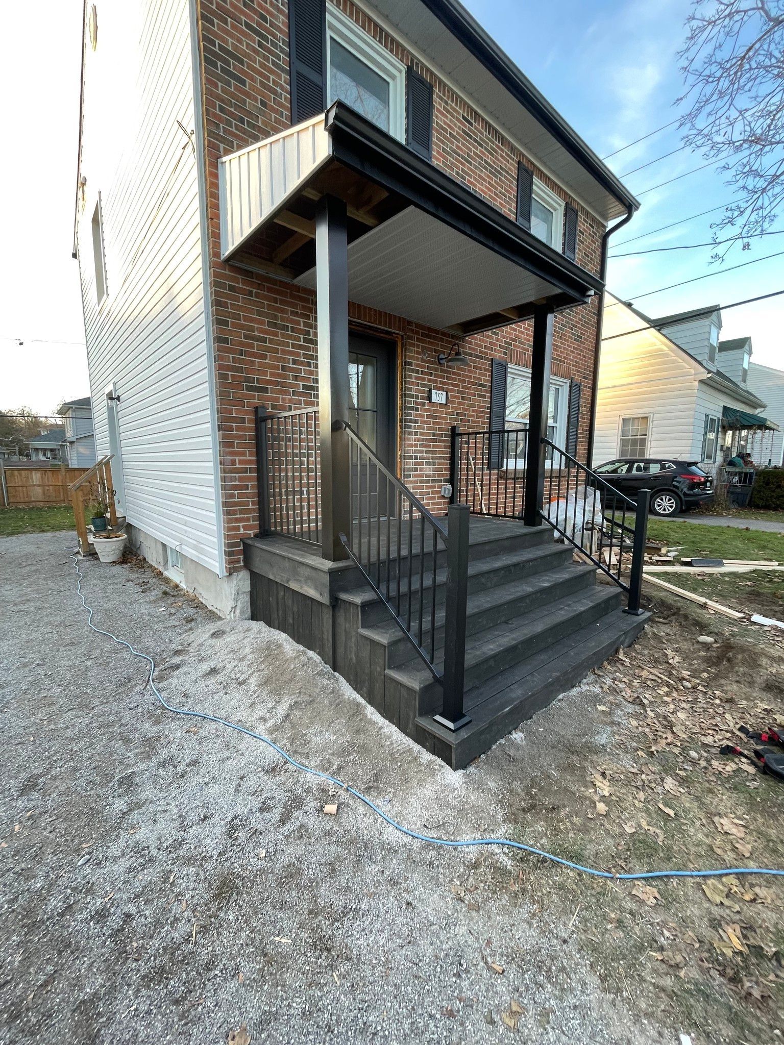 A two-story brick building with a newly constructed dark gray porch and steps. Black railing, gravel yard.