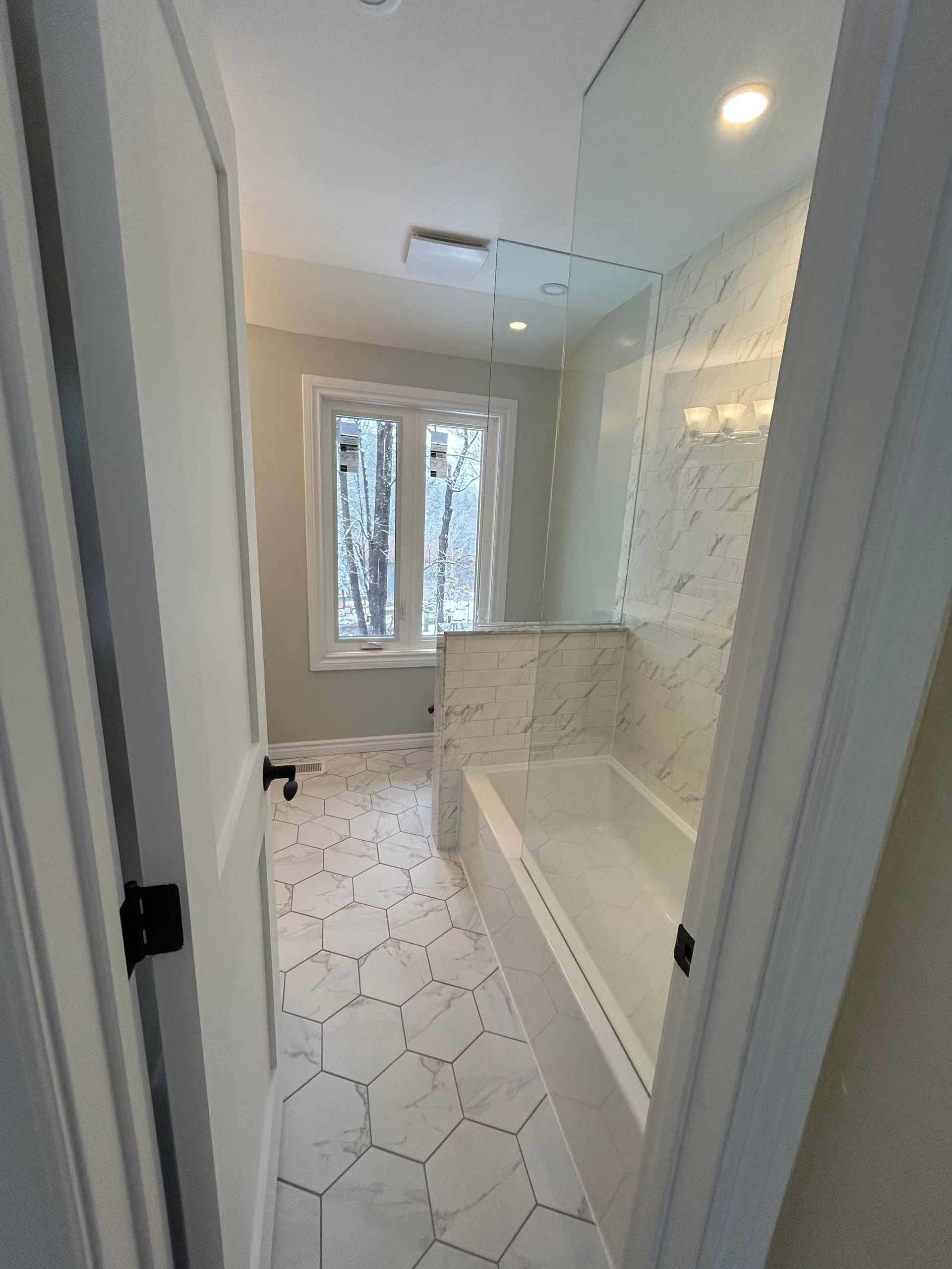 Bathroom with white hexagon floor tiles, tub, and tiled shower wall. Window provides natural light.