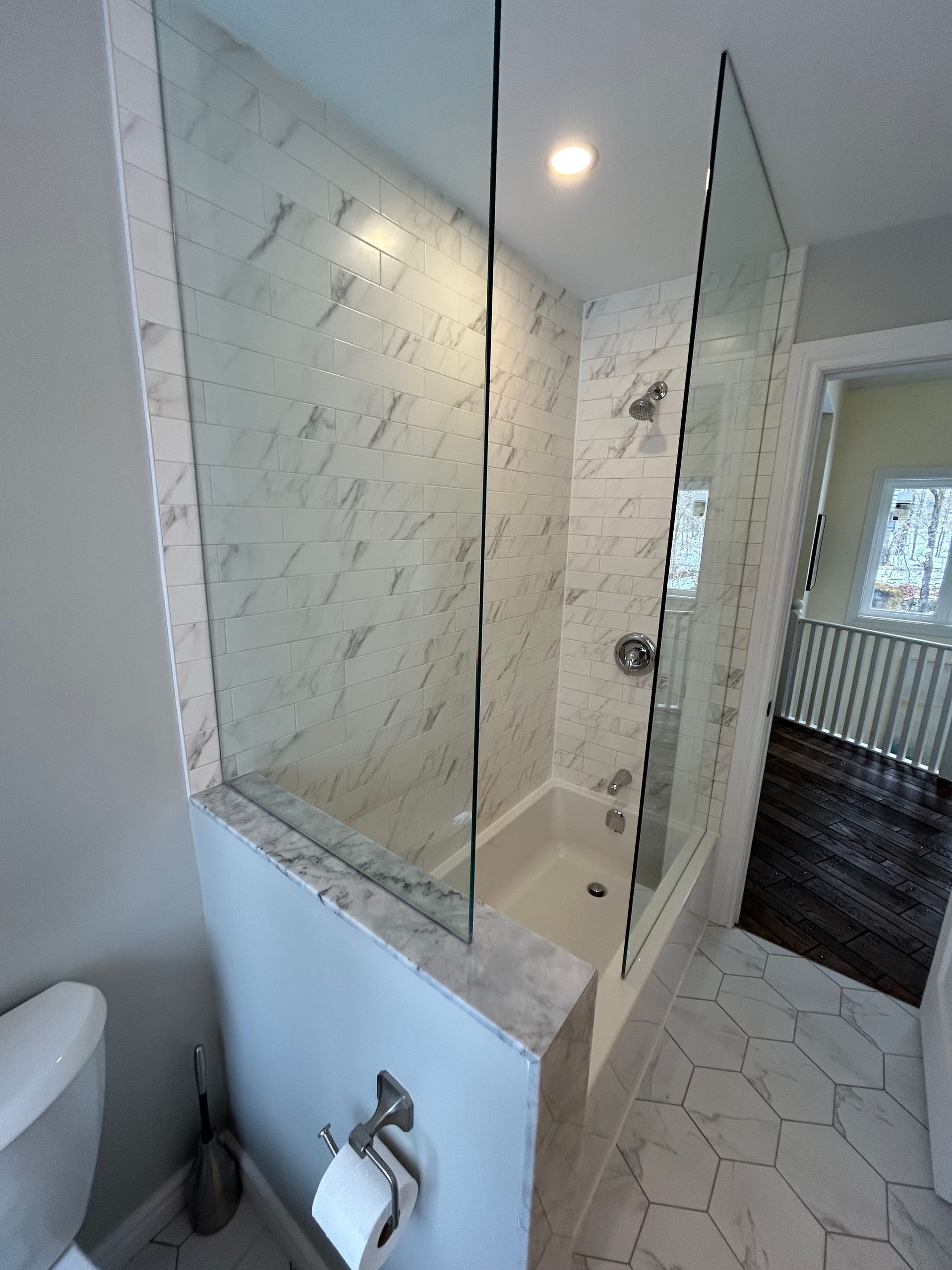 Bathroom with a glass shower enclosure and marble-look tiles.