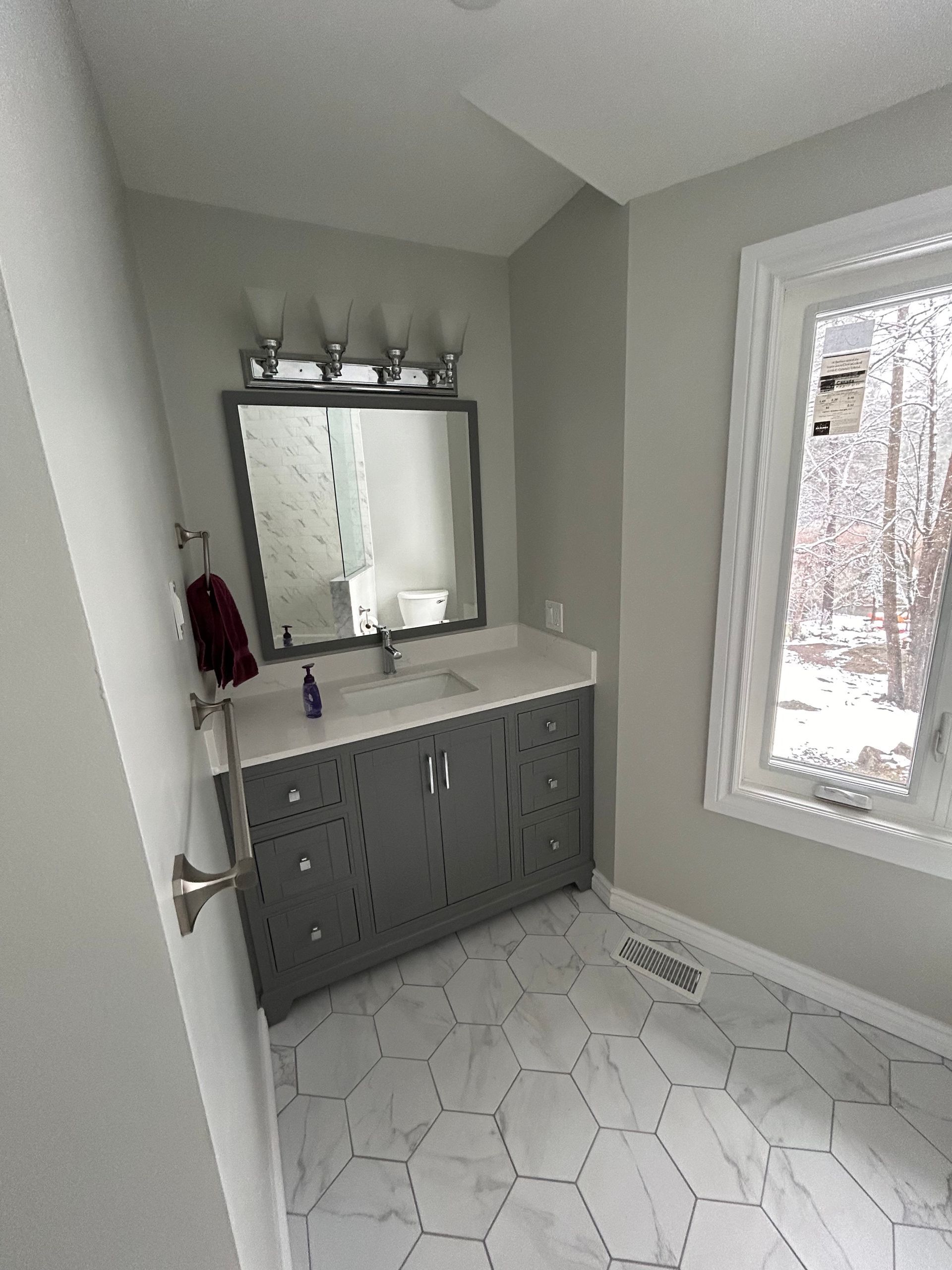 Gray bathroom with vanity, mirror, window, and hexagonal floor tiles.
