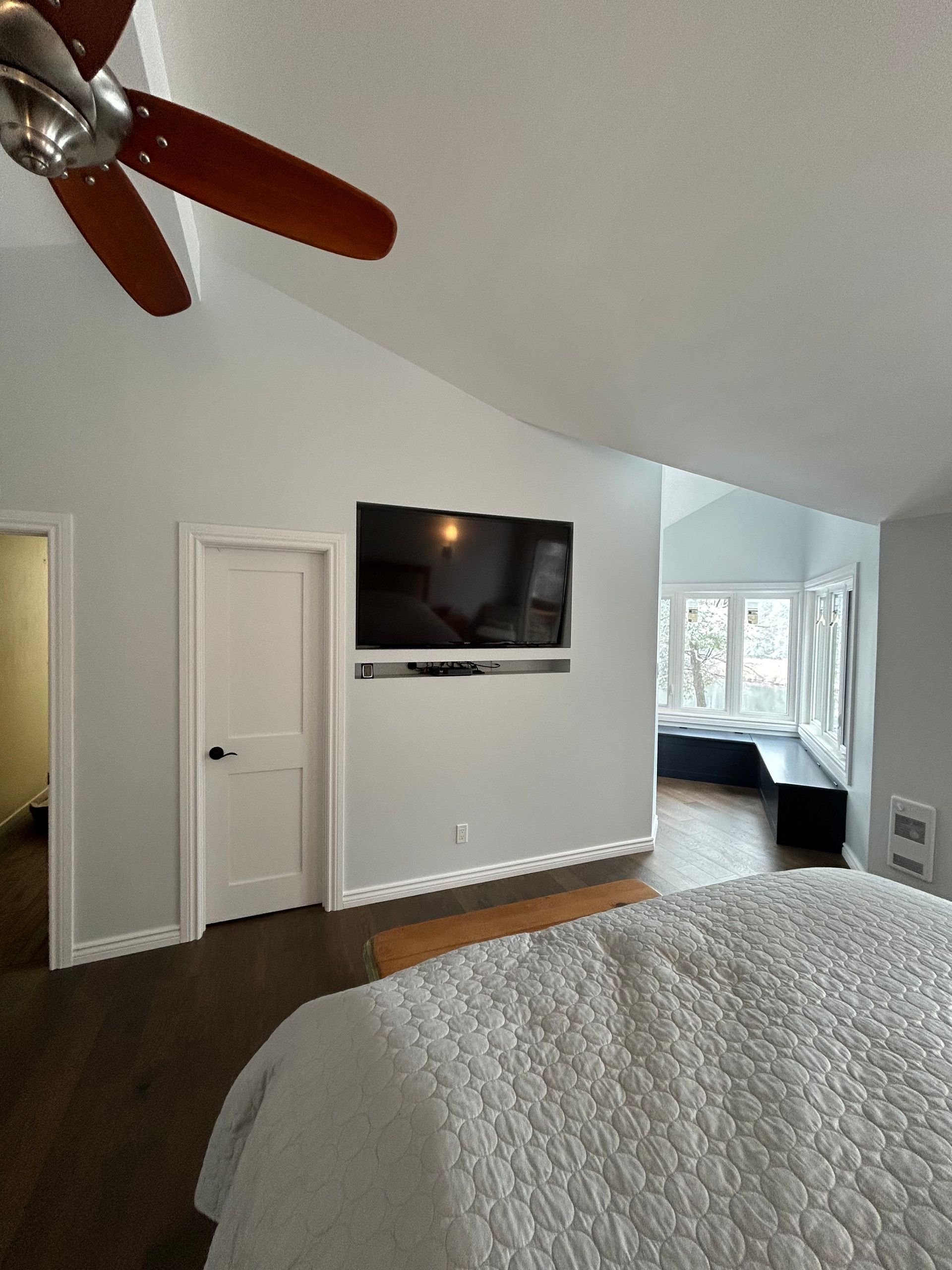 Bedroom with mounted TV, door, and bench seating. The ceiling is angled.