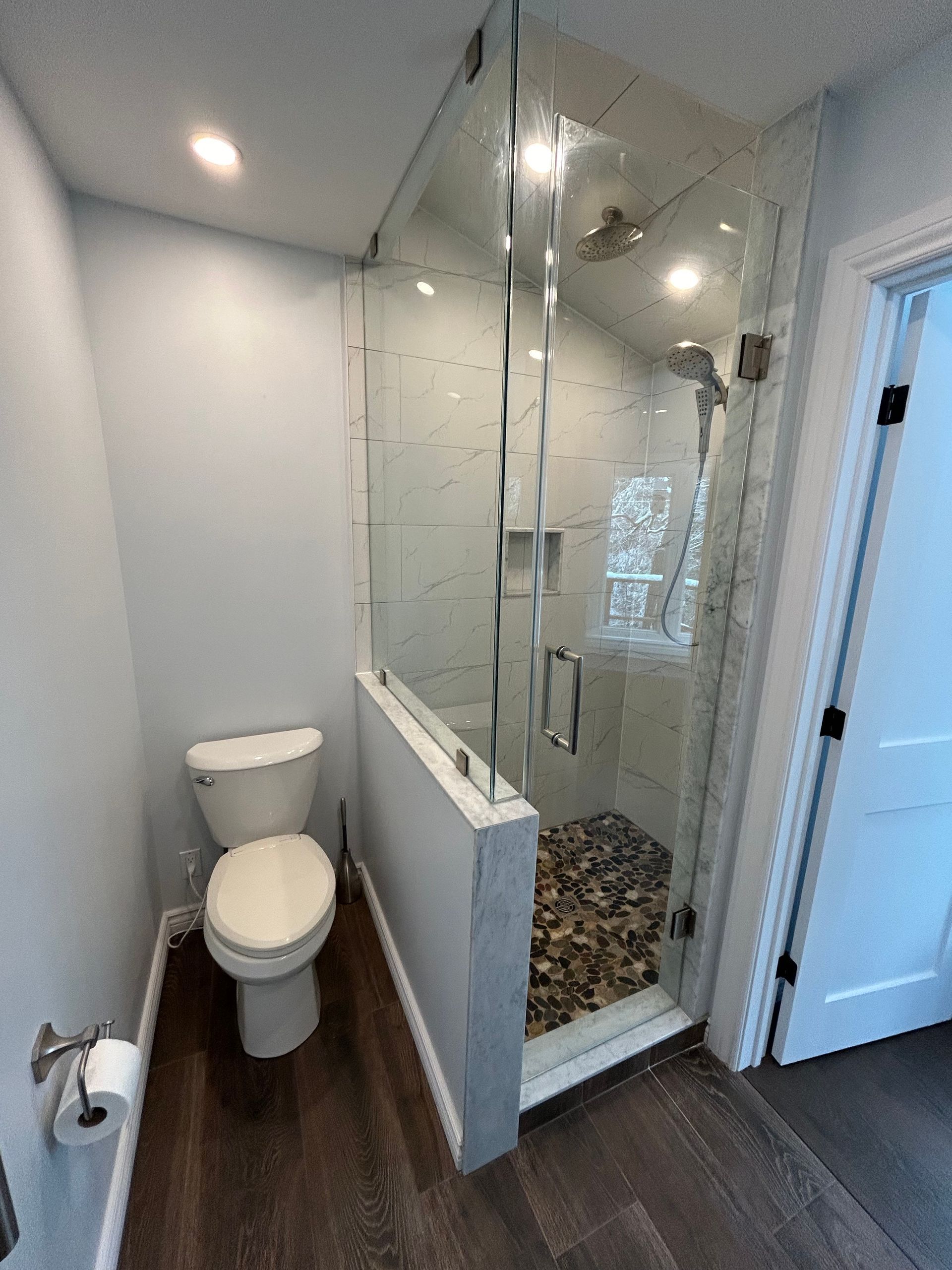 A small modern bathroom with a glass shower, toilet, and wooden floor.
